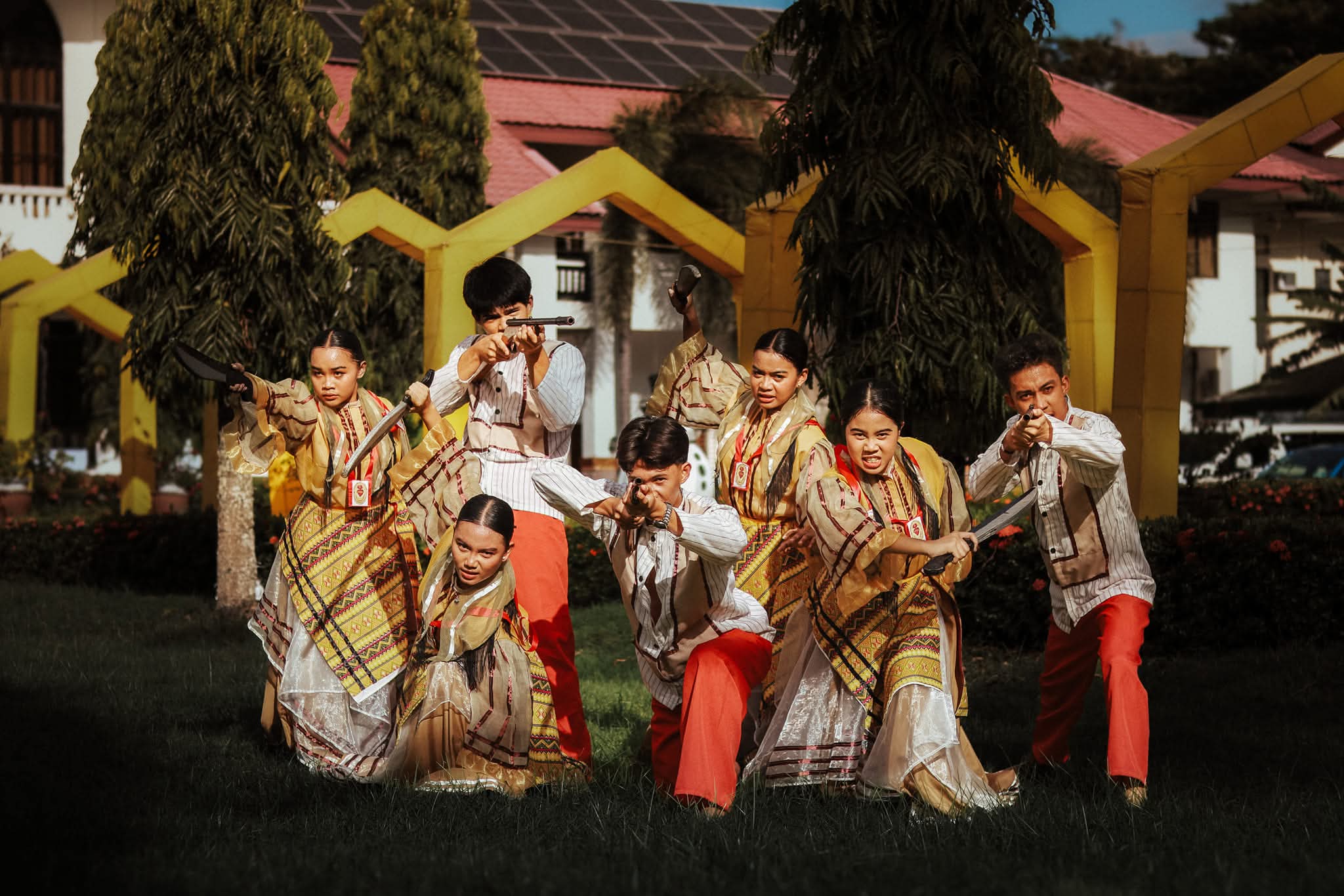 Performers in low combat lunge poses on the festival lawn, weapons drawn.